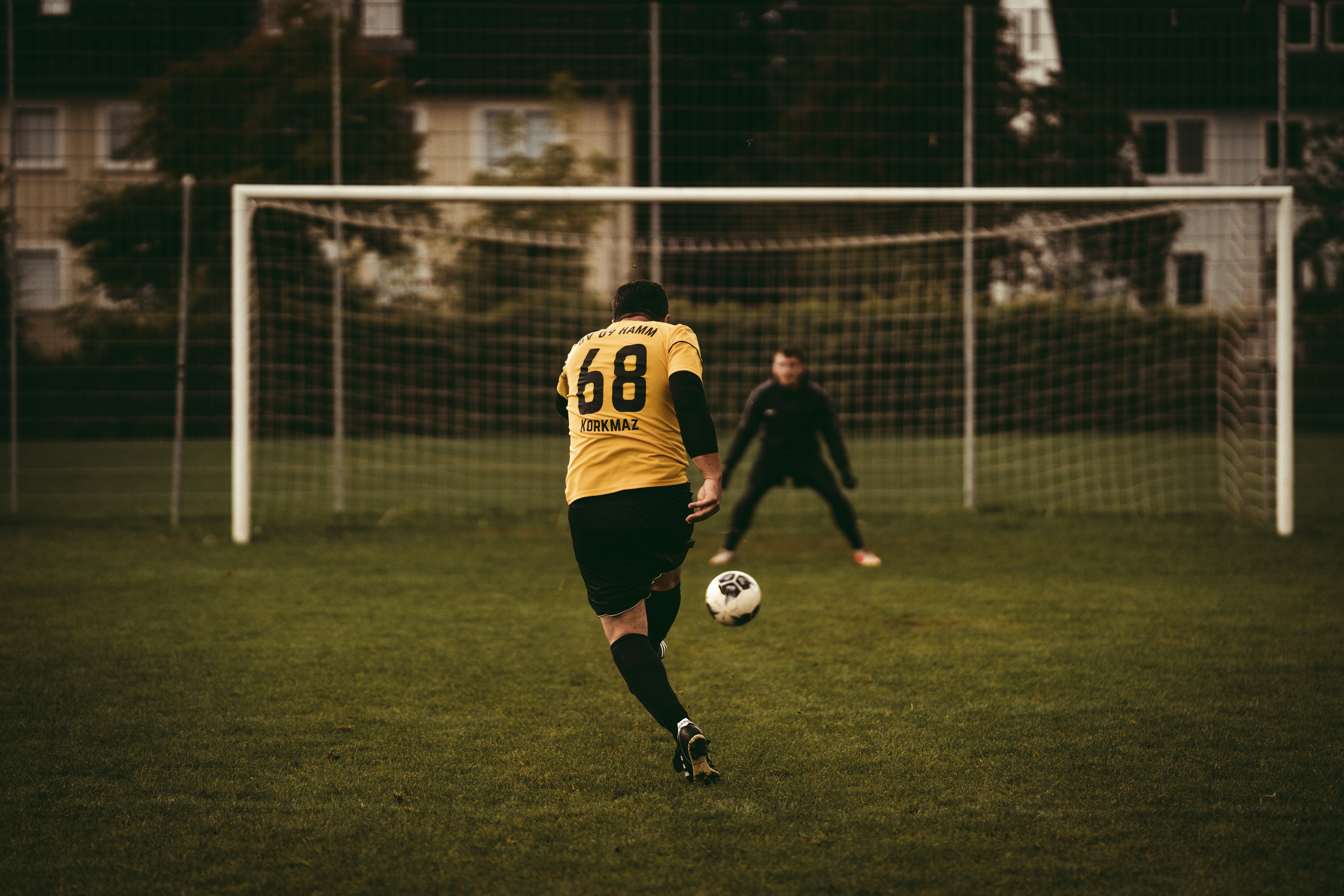 man in yellow and black soccer jersey kicking soccer ball on green grass field during daytime
